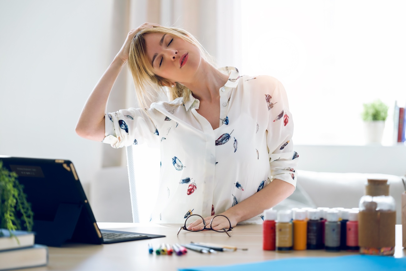 Female stretching her neck while sitting at desk working on laptop