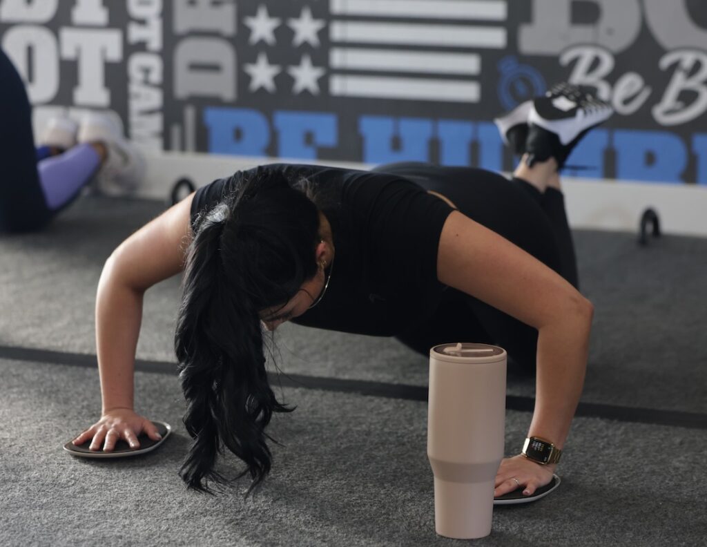 Woman using pushup slide plates to improve form at a Fit Body Boot Camp class.