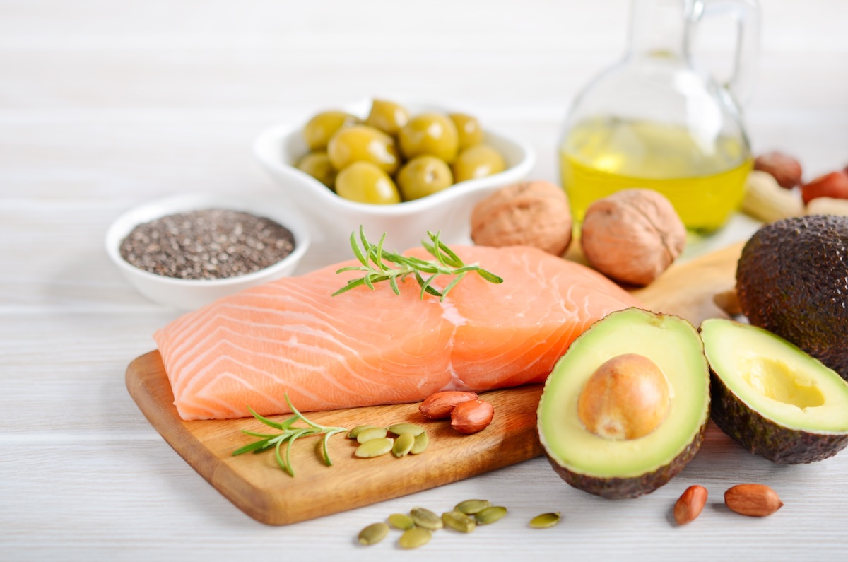 Collection of foods with health fats including salmon, nuts, and avocados.