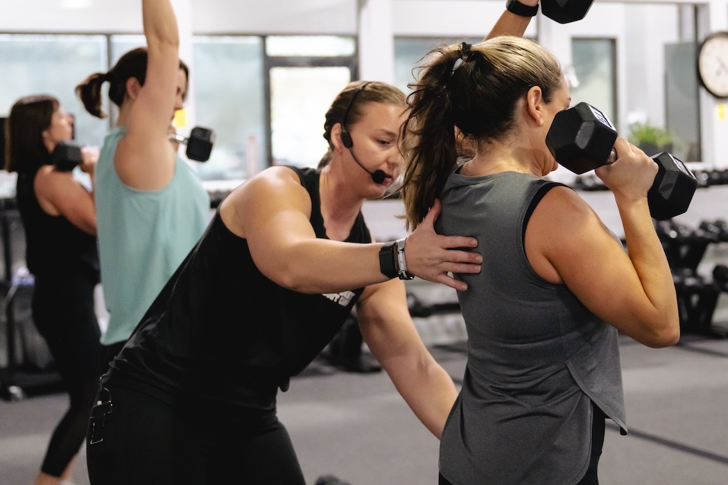 Fitness coach working with Fit Body Boot Camp member to adjust form.