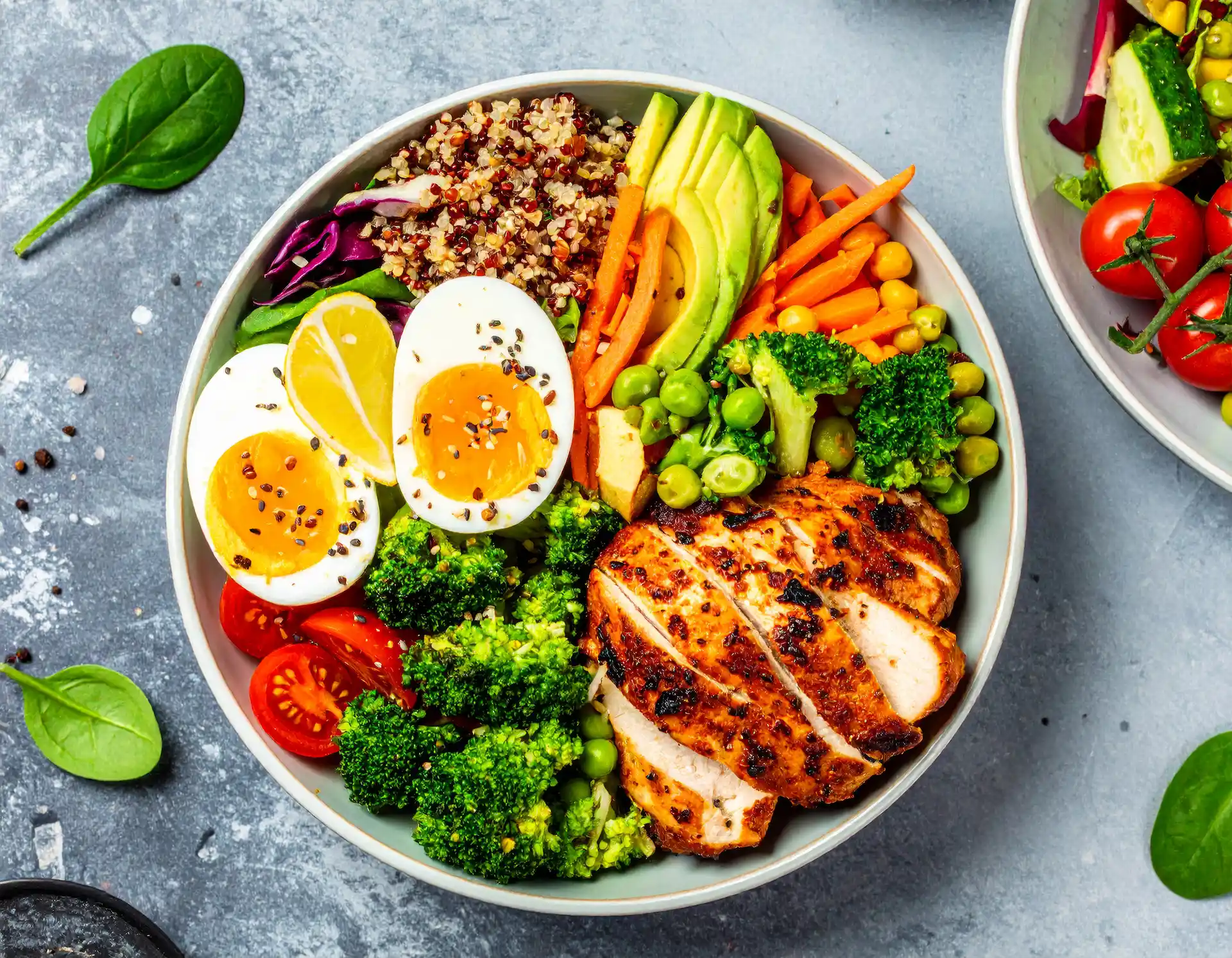 Healthy nutritional bowl with eggs, avocado, carrot, chicken breast, and quinoa.