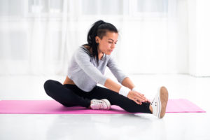Fit woman doing aerobics gymnastics stretching exercises her leg and back to warm up at home on yoga mat