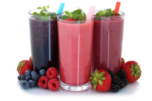 healthy strawberry, blueberry, and raspberry smoothies in glasses with colored straws